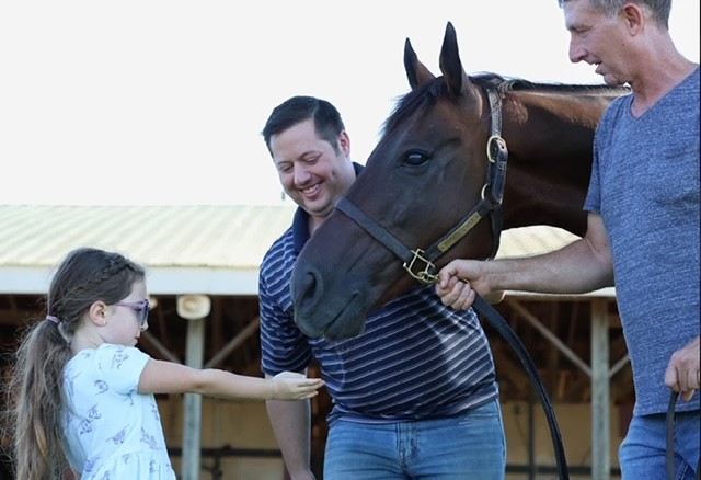 Two men and a girl holding out her hand towards a horse