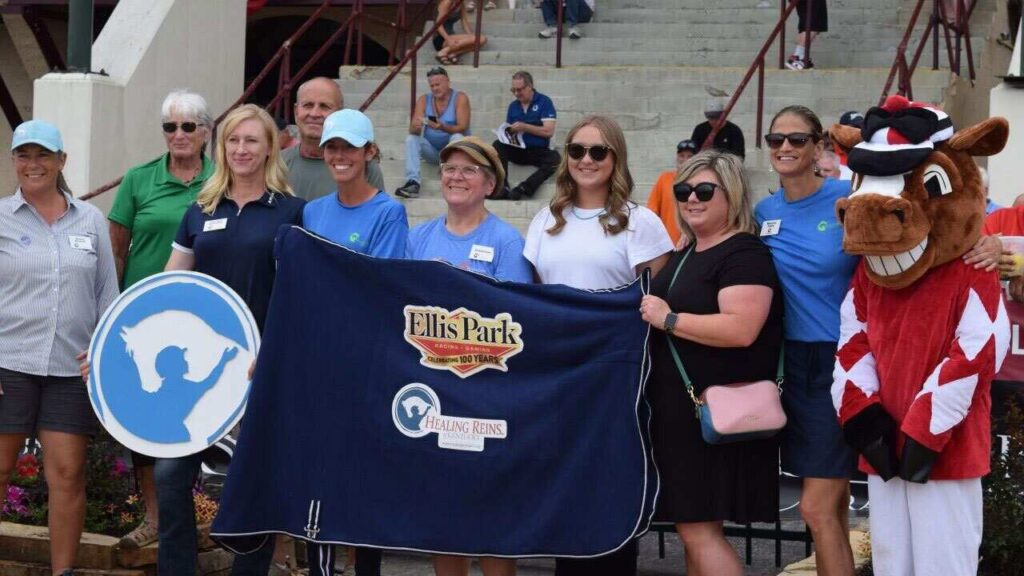 People holding an Ellis Park Racing & Gaming blanket that says Celebrating 100 years